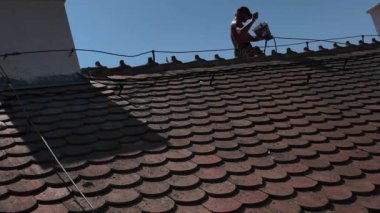 Bir işçi çatıya tırmanıyor ve bacayı onarıyor. Bir işçi çatıyı tamir eder. Çatıda güvenlik ipi ve çatı emniyet kemeri olan bir işçi var. İnşaat işi ve yükseklerde çalışma kavramı.