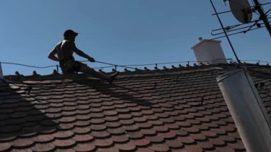 Eski kil kiremit çatısının tepesinde çalışan bir işçi. Bir işçi çatıyı tamir eder. Çatıda güvenlik ipi ve özel emniyet kemeri olan bir işçi. İnşaat işi ve yükseklerde çalışma kavramı.