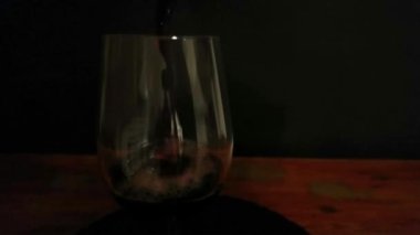 Bir bardağa kırmızı şarap dolduruyorum. Karanlık bir arka plana şarap dökmek. Ağır çekim. Gastronomi ve aşçılık kavramı.