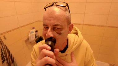 Gözlüklü yaşlı bir adam banyoda tıraş oluyor. Bir adam tuvalette tıraş makinesiyle tıraş olur. Gözünde çürük olan bir adam. Kişisel bakım kavramı..