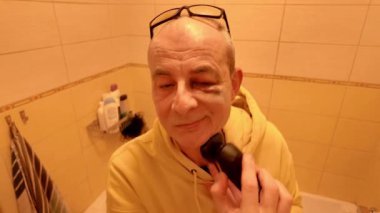 Yaşlı bir adam duşta elektrikli jiletle tıraş olur. Gözlüklü yaşlı bir adam banyoda tıraş makinesiyle tıraş oluyor. Gözünde çürük olan bir adam. Günlük rutin konsept ve