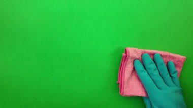 Lastik eldivendeki bir el pencere camını siler. Lastik eldivendeki bir el yüzeye sürtünür. Yeşil krom anahtar arka plan. Ev işi ve temizlik kavramı.