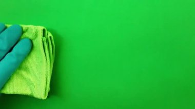 Yeşil bir bezle yüzeyi siliyorum. Cam pencereyi mendille ovmak. Yeşil lastik eldivenli bir kadın eli yeşil bir ekranın arka planına karşı kuru bir bez ile pencerenin camını siler.