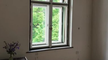 Eski moda ahşap pencereye doğru yürür ve onu sonuna kadar açar. Odada eski moda pencereler var. Eski zaman ve romantizm kavramı.