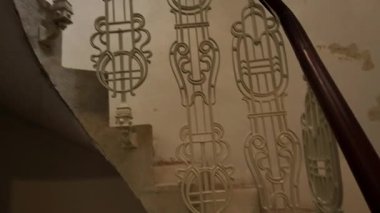 Tarihi bir binanın tarihi sarmal merdivenlerinden aşağı iniyor. İşlenmiş demir parmaklıklı sarmal merdiven. Tarihi ve mimari miras kavramı.