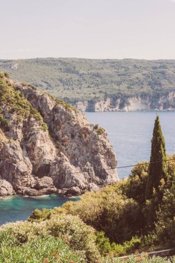 Korfu, Yunanistan. Büyük dağlar ve yeşil ağaçlarla kaplı mavi sulardaki gri kayalar manzaralı güzel bir manzara..