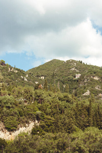 Corfu, Greece. The mountain is overgrown with green trees against a blue sky.