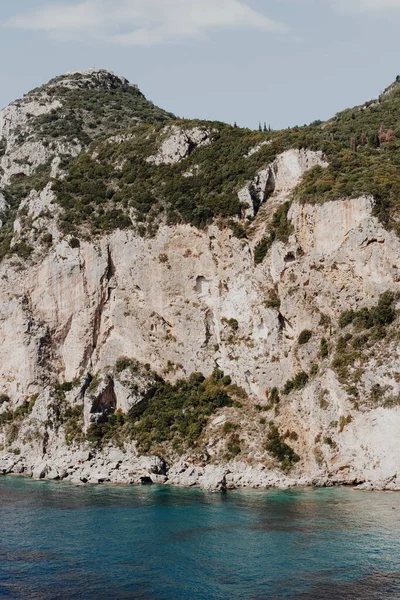 ギリシャのコルフ 夏の太陽が輝く美しい青い水によって緑の植物が成長する巨大な山の岩 — ストック写真