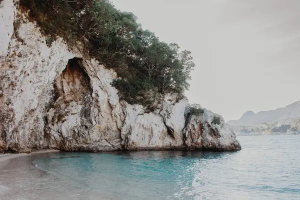 ギリシャのコルフ 緑の植物や木が育つ青い水のビーチの巨大な岩 — ストック写真