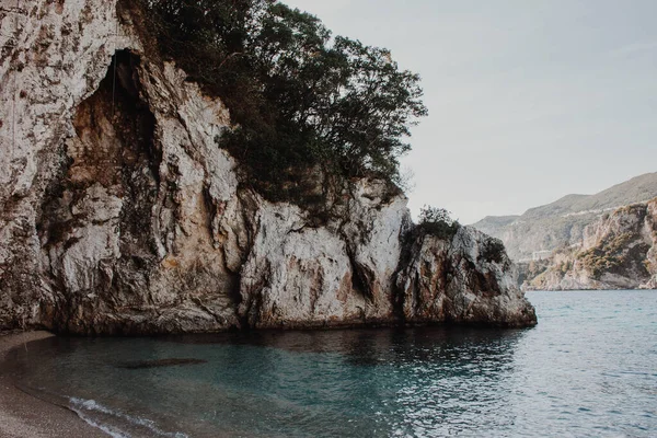 Korfu, Yunanistan. Sahilde yeşil bitki ve ağaçların yetiştiği mavi suyu olan dev bir kaya..