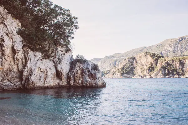 ギリシャのコルフ 緑の植物や木が育つ青い水のビーチの巨大な岩 — ストック写真