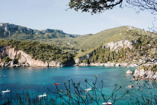 ギリシャのコルフ 緑の植物や木々が生い茂る巨大な山の岩が青い水の横に見え モーターボートが立っている — ストック写真