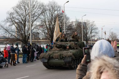 18.11.2022 Riga, Letonya. Ulusal tatillerde askeri geçit töreni. Askerler bir tankın içinde araba kullanırlar ve kalabalıklar onu caddenin kenarında seyrederler..