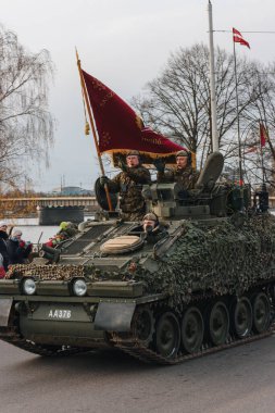 18.11.2022 Riga, Letonya. Ulusal tatillerde askeri geçit töreni. Askerler bir tankın içinde araba kullanırlar ve kalabalıklar onu caddenin kenarında seyrederler..