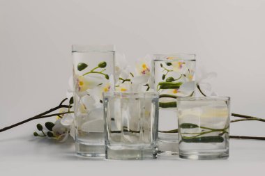 Önünde su dolu cam bardaklar olan beyaz arka planda beyaz çiçeklerle dolu bir hayat bir illüzyon yaratır..