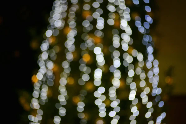 Blurred multicolored lights of a garland and branches of a Christmas tree in the foreground.Christmas and New Year background.Selective focus,copy space.