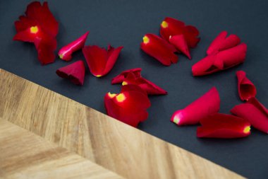 Red rose petals on a black background next to a wooden board for cooking.