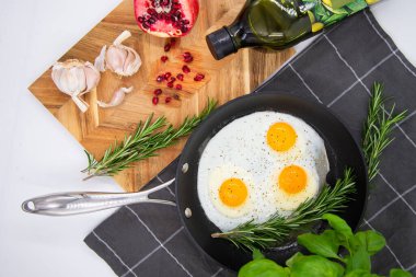 breakfast or brunch, fried eggs in black pans and red pomegranate with garlic and basil. view from the top.