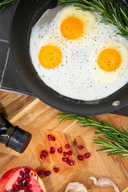 breakfast or brunch, fried eggs in black pans and red pomegranate with garlic and basil. view from the top.
