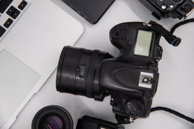 top view of work space photographer with digital camera, flash, cleaning kit, memory card, external hard disk, USB card reader, laptop and camera accessory on white table background