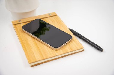 Mobile smart phone with blank screen of gadget on notebook. Digital cell phone with copy space area on white background with pencil and leaf