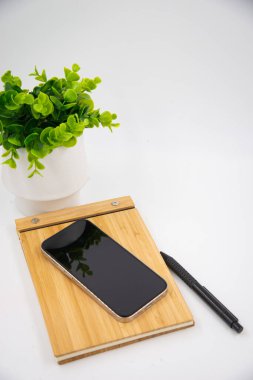 Mobile smart phone with blank screen of gadget on notebook. Digital cell phone with copy space area on white background with pencil and leaf