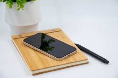 Mobile smart phone with blank screen of gadget on notebook. Digital cell phone with copy space area on white background with pencil and leaf