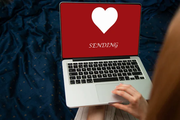 Hand holding laptop with sending word and heart shape on screen on light bokeh background, Happy Valentine\'s Day
