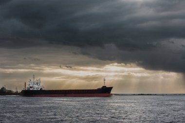 Denizi aşan tankerin görüntüsü dramatik bir karanlık gökyüzünün altında altın güneş ışığı bulutlarda parlıyor..