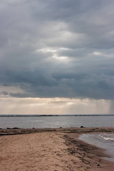 海滨有一个沙堤 通往防波堤 戏剧化的天空 云层中闪烁着太阳光 — 图库照片