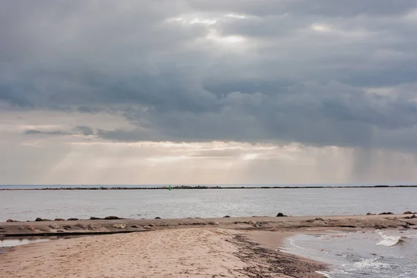 海滨有一个沙堤 通往防波堤 戏剧化的天空 云层中闪烁着太阳光 — 图库照片