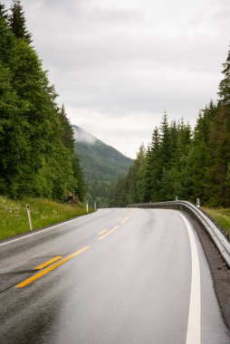 Yazın yağmurlu bir günde dağ yolunda. Norveç. Güzel kıvrımlı yollar, kayalar, taşlar, bulutlu mavi gökyüzü. Baharda dağ geçidinden geçen içi boş otoban manzarası. Seyahat