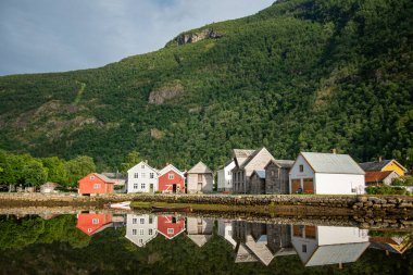 concrete bridge over a river with water like a mirror reflecting the beautiful Norwegian fjord mountains in the village of which is the administrative center in Vestland County, Norway. clipart