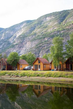 NORWAY - July 8, 2023: Norwegian campsite with small orange wooden houses by the river at the foot of the mountains in the village of Lrdalsyri, which is the administrative center of Lrdal Municipality in Vestland County, Norway clipart