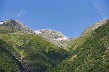 Norwegian mountain landscape where the mountain divides into several layers. Snow on the top of the fjord under a blue summer sky. clipart