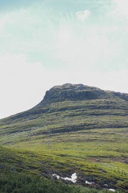Norveç 'te, güneşli bir yaz gününde mavi gökyüzünün altında yeşil ağaçların büyüdüğü bir dağ manzarası..