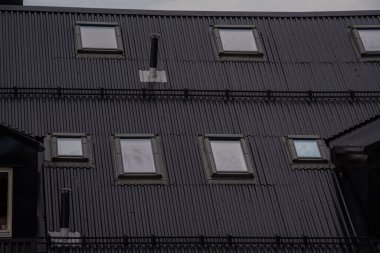 Oslo, Norveç - 11 Temmuz 2023: Çatı pencereleri ve havalandırma bacası olan bir apartmanın siyah metal çatısı.