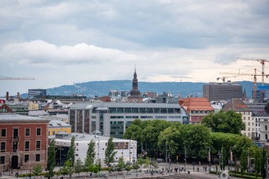 Oslo, Norveç - 12 Temmuz 2023 - Norveç şehir merkezi manzarası. İnşaat için görünen vinçleri olan binalar ve uzakta büyük bir dağ var..