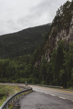 Norveç dağ manzarası, asfalt bir yol ile uçurumun kenarından metal güvenlik bariyerleriyle ayrılmış sarı çizgiler bir sonbahar günü.