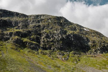 Norveç dağlarının kayalık dağları mavi gökyüzünün altında beyaz kümülüs bulutlarıyla.
