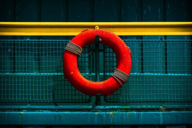 Bright Red Lifebuoy Mounted on a Colorful Rail with Industrial Backdrop clipart