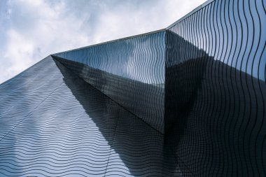 Dalga benzeri desenlere ve yansıtıcı tasarım elementlerine sahip açısal cam cepheleri içeren çağdaş mimari kavram