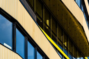Kentsel Ayarlarda Yansıtıcı Pencereleri ve Altın Aksan Panelleri olan Modern Cam Bina