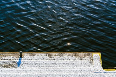 Snow-Covered Wooden Pier by Calm Blue Water with Sunlight Reflections on the Surface clipart