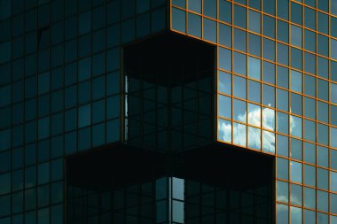 Derin yansımaları ve turuncu pencere ızgarası olan modern cam bina keskin bir geometrik bileşim oluşturuyor.