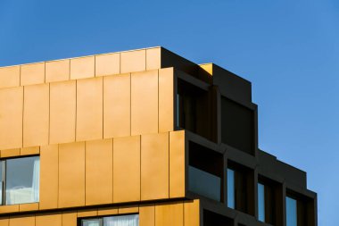 Parlak mavi gökyüzüne karşı koyu güneş ışığı ve derin gölgelerle zigzag çizen sarı balkonlar.