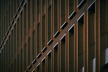 Sıcak güneş ışığıyla aydınlatılan ve güçlü geometrik karşıtlık ve ritim yaratan, tekrarlayan dikey pencerelerle modern bina sessizleşir