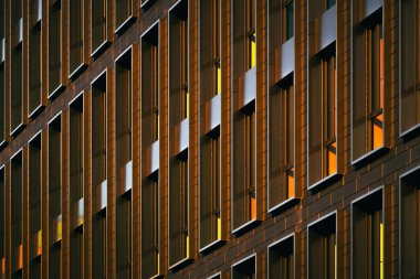 Sıcak güneş ışığıyla aydınlatılan ve güçlü geometrik karşıtlık ve ritim yaratan, tekrarlayan dikey pencerelerle modern bina sessizleşir