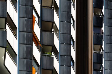 Çağdaş konut kulesinin geometrik cephesinde tekrarlanan balkonlar ve pencereler sarı aksanlı paneller yer almaktadır.