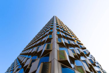 Modern residential building facade with geometric bay windows and reflective blue glass creating dynamic architectural texture